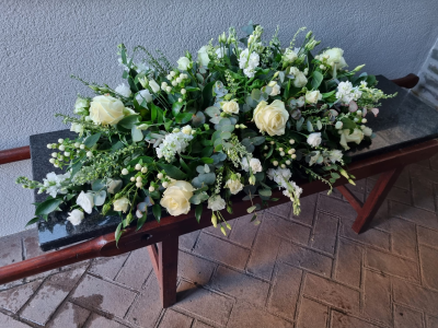Casket Spray - White - A beautiful classic tribute using a mix all white seasonal flowers with green foliage. Please call before ordering to discuss if there are specific flowers you would like.